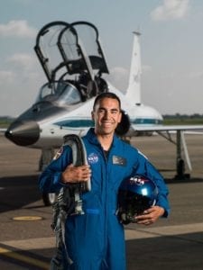 Raja Chari, Eagle Scout and member of 2017 NASA Astronaut Candidate Class, smiles in front of jet, wearing blue NASA flight suit.