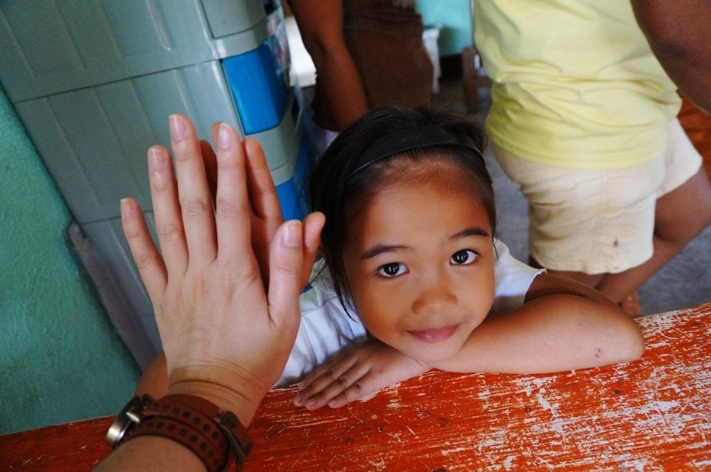 A small, cute girl looks up as she high-fives another volunteer.