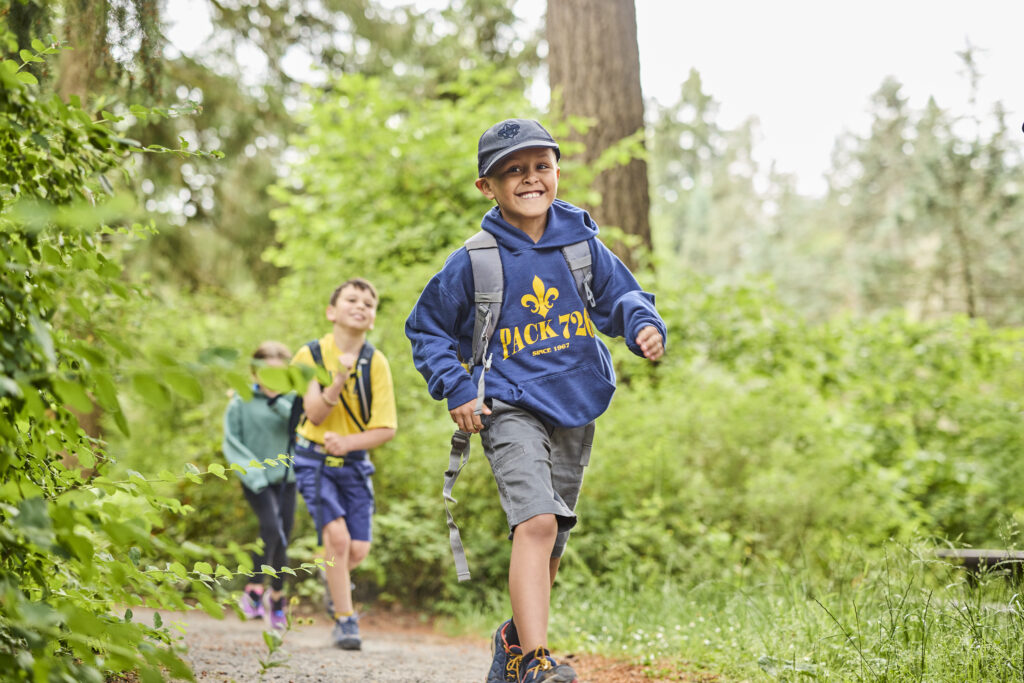 Cub scout smiling while hiking along a trail in the forest. 