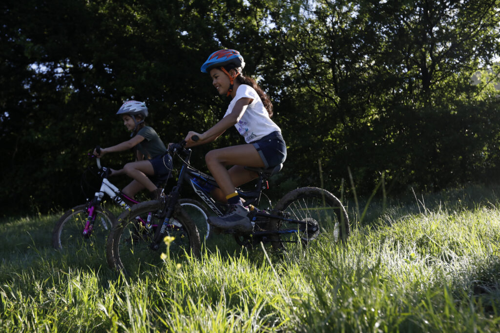 Two girls on an outdoor adventure, riding their bikes through the grass. 